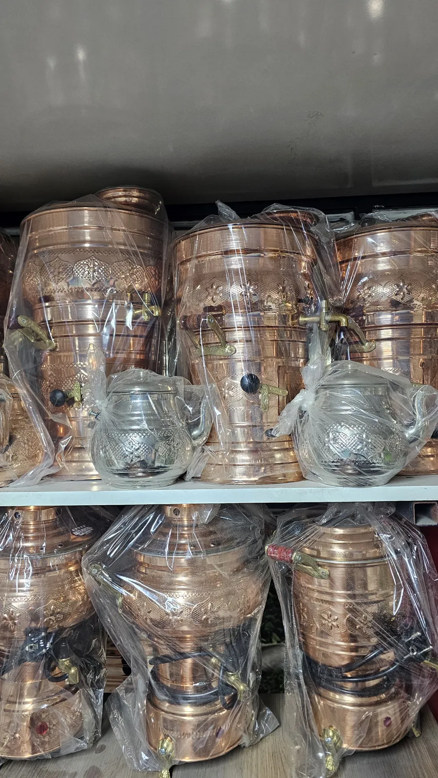 Rafta dizili paketli bakır ve gümüş renkli semaverler ile demlikler